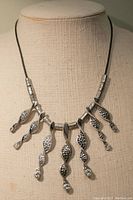 Front view of the black cord necklace with silver etched drop pendants adorned with rhinestones hanging down, displayed on a mannequin bust.