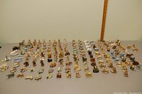 Wide shot of the entire collection of small figurines laid out in rows on a table with a measuring stick in background