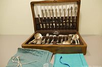 Chest open showing satin‐lined knife slot, felt tray of silverware and two cloth pouches in front