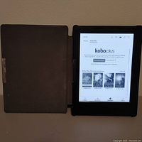 Photo of Kobo Aura H2O e-reader powered on showing Kobo Plus interface with opened sleep cover in black color.