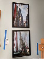 Two vertically arranged framed paintings showing sailboat masts, rigging, and nets in a maritime scene