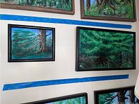 Two framed landscape paintings depicting trees and forest greenery hung on a wall, each painted by Donald Gotz.