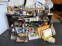 Overview of shelves containing assorted art supplies including wood stains, adhesives, brushes, cords, and packaging materials.