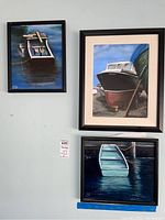 Three framed boat paintings displayed on a wall: one small square boat painting, one medium large vertical boat painting, and one smaller square blue boat painting.