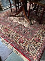 Photo showing a section of the area rug with detailed traditional pattern and worn fringe visible along one edge.