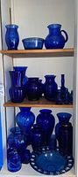 Shelf with assorted cobalt blue glassware including pitchers, bowls, vases, canisters, and serving dish