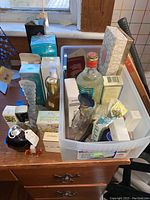 Wide view of tote containing multiple perfume and cologne bottles and boxes on wooden dresser by window.