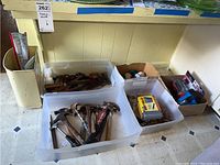 Overhead shot of multiple plastic bins containing hammers, various hand tools including snips and screwdrivers, and batteries taken to show assortment and condition of tools.