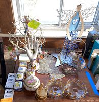 Photo showing a variety of trinket boxes in floral patterns, a ceramic hand figurine, a wire angel basket in blue, and a wired jewelry tree holding jewelry