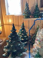Four green ceramic Christmas trees in varying sizes displayed on table with bag of bulbs visible