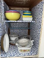 Various vintage mixing bowls and bakeware displayed inside and just outside a cupboard with blue floral interior.