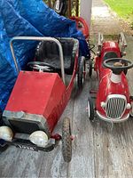 Two vintage push cars side by side on wooden porch floor showing front and back views