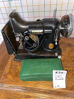 Front-left perspective of sewing machine with motor, foot pedal and green Singer attachment box
