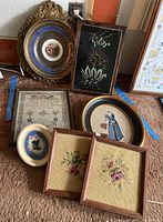 Overview of all seven pieces of wall art including ornate plaque and framed needlepoints.