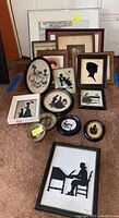 View of the full collection of framed silhouette and religious themed wall art on carpet, showing variety of frame shapes and sizes