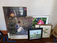 Grouping of six framed pictures leaning against a wall including a large Museum of Fine Arts Boston poster and floral prints