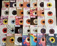Various 45 RPM records with paper sleeves and different label designs, showing condition and assortment.