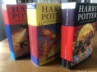 Three Harry Potter first edition hardcover books with dust jackets stood upright showing their side spines and front covers in part.