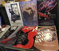 Six original Broadway play posters displayed together; The Producers, Brigadoon, Smokey Joe's Cafe, La Cage Aux Folles, The Life and West Side Story. Some posters are in plastic holders.