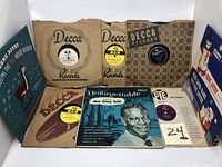 Displayed eight vintage 10-inch 78 RPM records in various original sleeves, some with colorful picture sleeves and artwork.