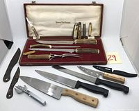 Photo showing Hudson Bay Company carving set with antler handled carving knife, fork, and sharpening steel in presentation box, pocket knives, forged blades, kitchen knives, can opener and other utensils arranged in front.