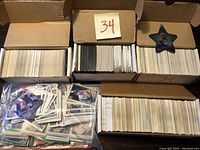 Three boxes filled with large quantities of mixed sports cards, mostly football and basketball, some baseball cards. One box clearly labeled '34'.