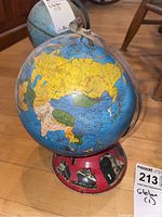 Front view of the vintage globe showing countries in yellow, blue, and green, mounted on a red metal stand with transportation motifs.