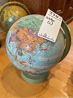 Full view of the vintage-style world globe showing Asia and surrounding continents, mounted on a green metal stand.