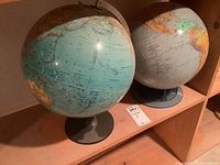 Two world globes on black stands shown together on a shelf.