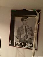 Framed black-and-white Mr. Bean vote poster hung on wall with other items nearby.