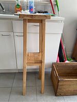 Front angled view of wood plant stand showing top surface, legs, and water damage