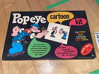 Box lid image showing the kit title and artwork of Popeye, Olive Oyl, and Bluto with text about the plastic shapes and ease of use.