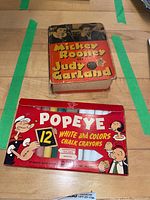 Photo showing vintage Mickey Rooney and Judy Garland book and Popeye chalk crayons box on table