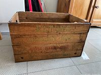 Side view of the rectangular wooden crate showing faded green and red text with eatons grocery box branding, natural aging and wear visible.