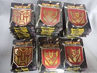 Multiple stacks of car emblems in black and red colors, packaged with black and yellow branded backing card.