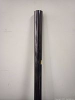 Single rolled black tinted solar window film standing vertically against a wall.