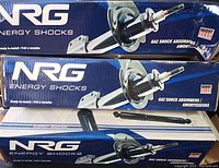 Three sealed NRG Energy Shock boxes stacked with two shocks and one smaller shock absorber visible outside the boxes.