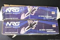 Two blue and white NRG Energy Shocks boxes sealed showing model packaging with images of shock absorbers and branding.