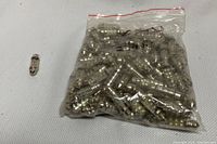 Bag of numerous small clear glass tube automotive lamp bulbs, with one bulb outside the bag to show detail.