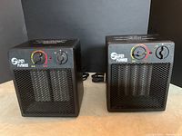 Two black Super Furnace space heaters side by side on a flat surface, front view showing controls and metal mesh grille.