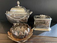 Three silver plate decorative items (flower frog, urn-style box, rectangular box) against a black backdrop