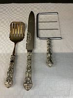 Three serving utensils with ornate Birks sterling silver handles displayed on a white textured cloth.