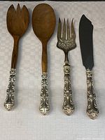 Four serving pieces with teak wood and sterling silver handles arranged on white cloth surface