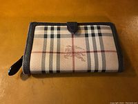 Front view of Burberry wallet showing plaid pattern, leather trim, and closure tab