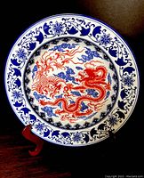 Full view of the porcelain charger plate displaying the red dragon motif with blue cloud and floral border patterns on a white background.