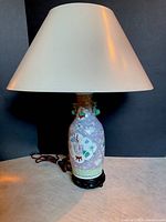 Front view of Chinese porcelain lamp with fabric lampshade and carved wooden stand, showing ornamental handles and detailed enameling.