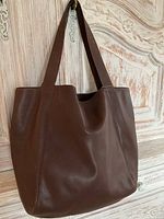 Front view of brown leather tote hung against wooden background.