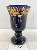 Full front view of the cobalt blue glass cup with gold ornamental detailing along the rim and upper body, showing the footed base.