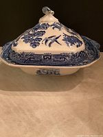 Side view of antique Blue Willow covered vegetable dish showing mismatched lid with ornate top handle and traditional blue pattern on white ceramic.