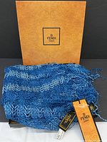 Blue open-knit scarf draped in front of Fendi branded box with original tags visible.
